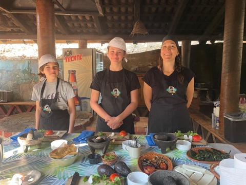 Tres participantes con mandil frente a una mesa llena de ingredientes bajo la palapa