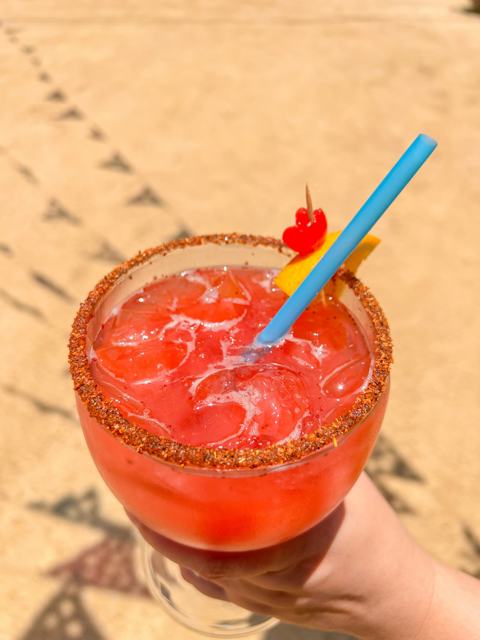 Bebida roja con hielo y popote en un vaso escarchado con chile