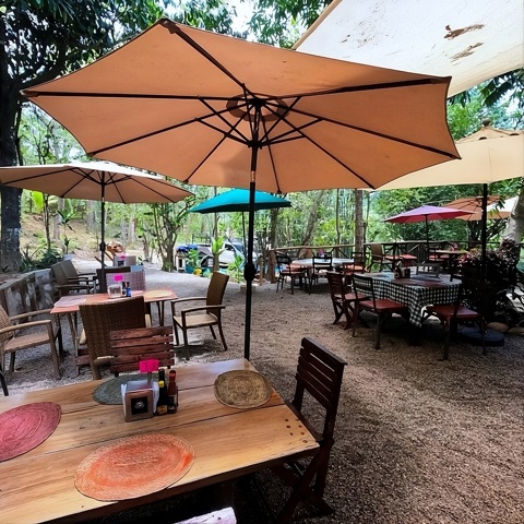 Restaurante al aire libre con sombrillas y mesas entre los árboles
