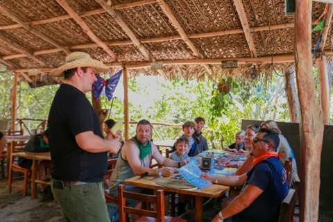 Guía con sombrero platicando con un grupo sentado a la mesa bajo la palapa